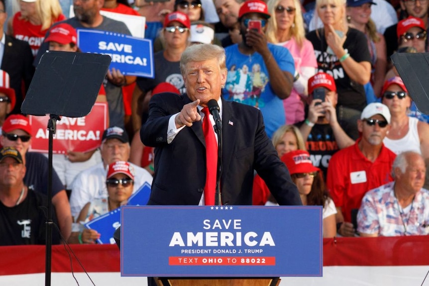 Former President Donald Trump addresses a rally, pointing at the gathered press and describing them as "Fake News"