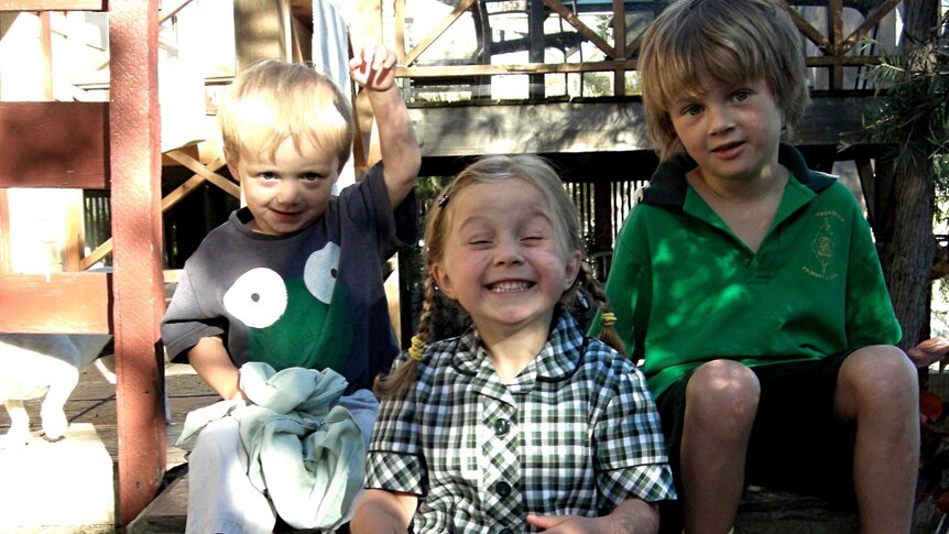 Three children smile big while sitting on steps
