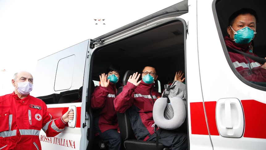 Medics and paramedics from China salute as the board a Red Cross vehicle upon arrival at an airport in Milan.