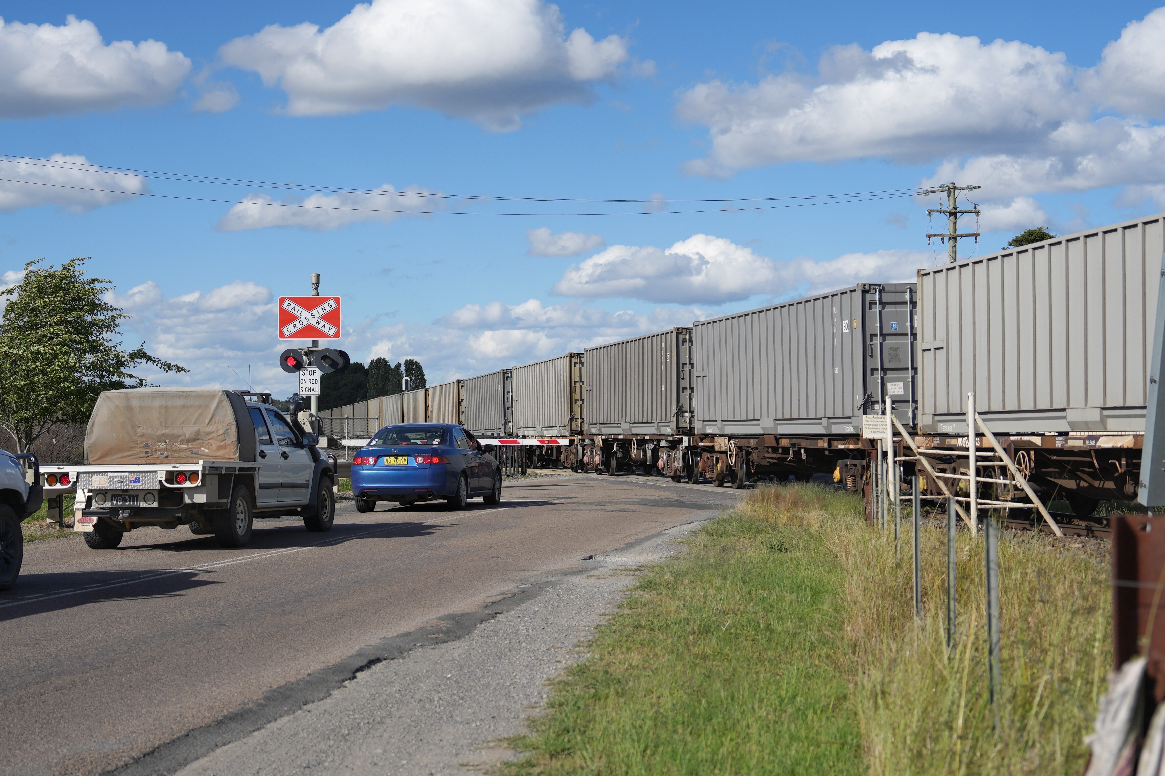 Un tren pasa por la ciudad mientras los coches esperan en las barreras.