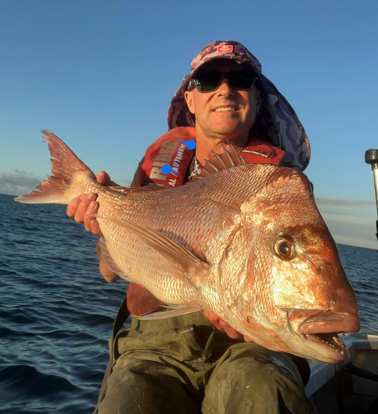 Fisher in a hat holds up a large red snapper out on a boat.