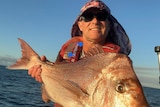 Fisher in a hat holds up a large red snapper out on a boat.