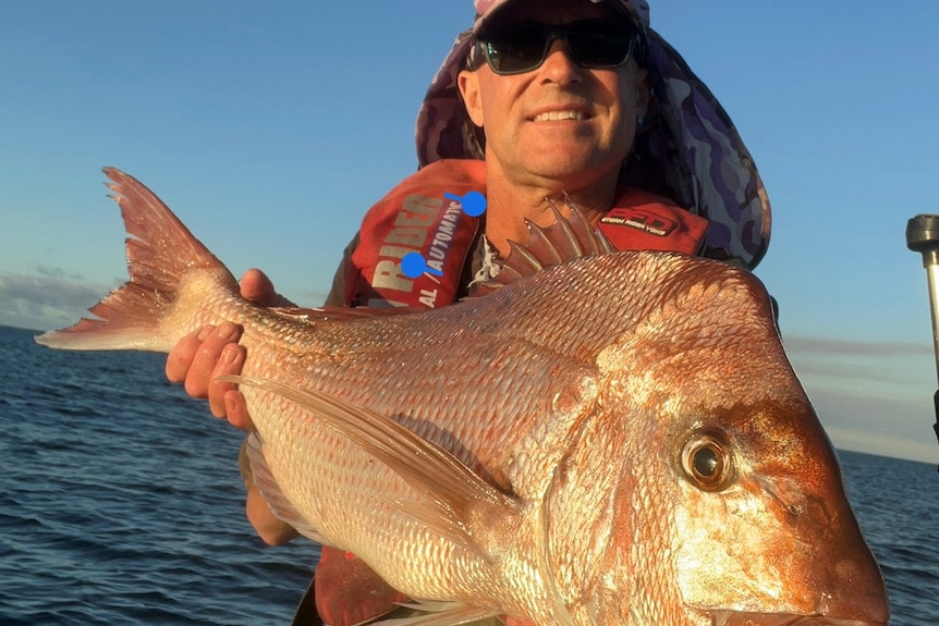 Fisher in a hat holds up a large red snapper out on a boat.