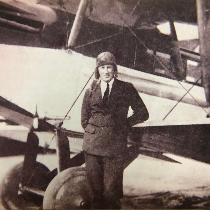 man in suit standing in front of an aeroplane on the tarmac.