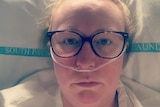 A woman wearing glasses lays in a hospital bed with a tube inserted into her nostrils.