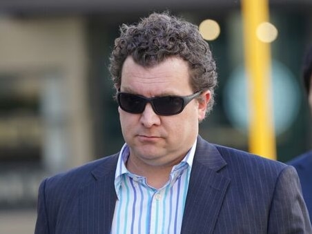 man in dark glasses with dark curly hair wearing striped shirt and jacket walks along street