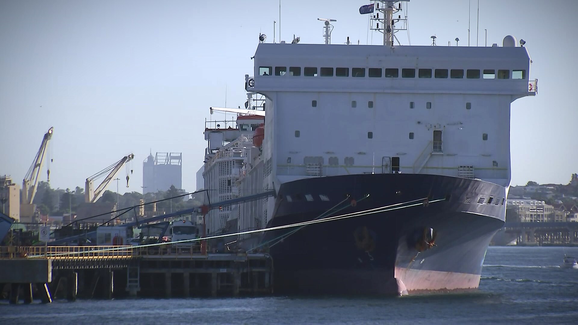 A ship in the water berthed at a port with Perth's skyline in the background