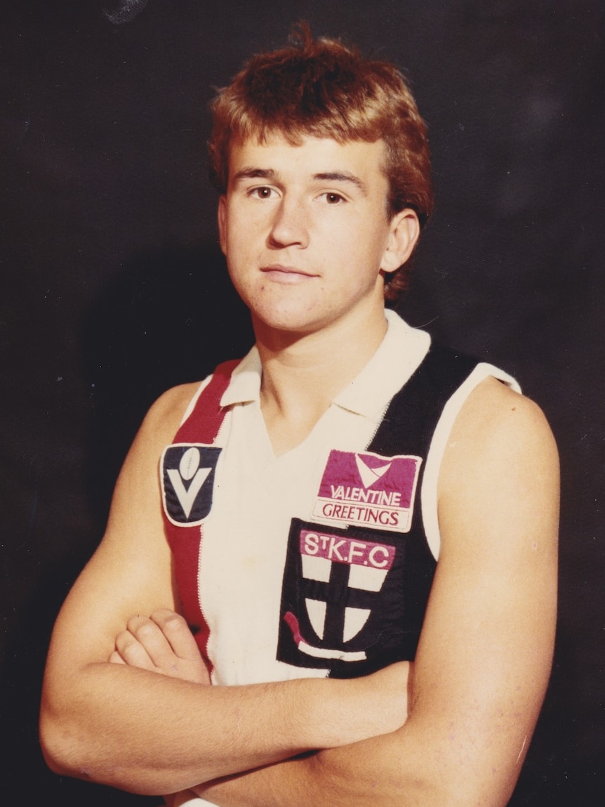 A teenage boy wearing a St Kilda jersey looks at the camera with his arms folded.