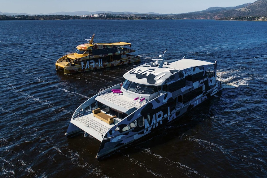 An aerial shot of two ferries in the water, both are decorated with an army camouflage design