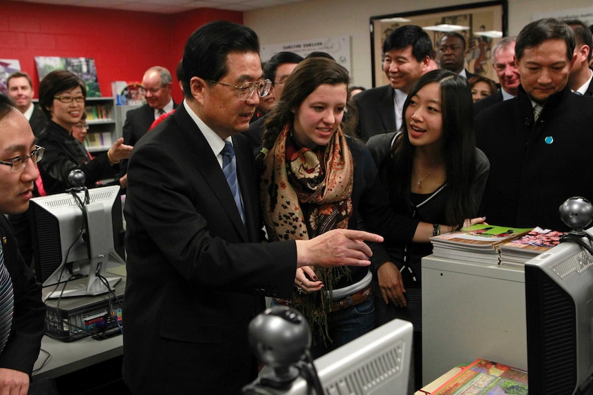 Former Chinese president Hu Jintao points at a computer while surrounded by people in a classroom.