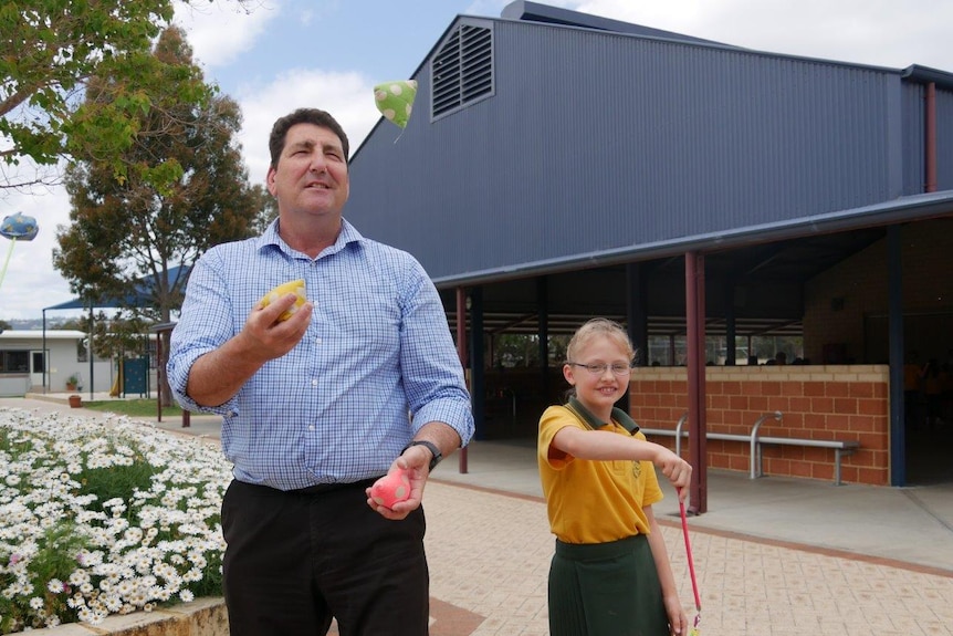A male teacher and young female student practising juggling and ribbon twirling in a school courtyard