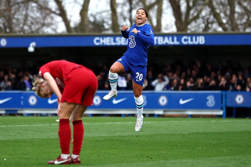 Sam Kerr jumps and punches the air after a goal against Liverpool. A red-clad player slumps in front of her.