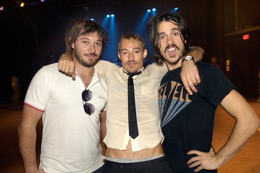 Three men smiling inside a music venue 