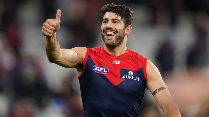 A Melbourne Demons AFL player smiles and gives the thumbs up with his right hand to the crowd.