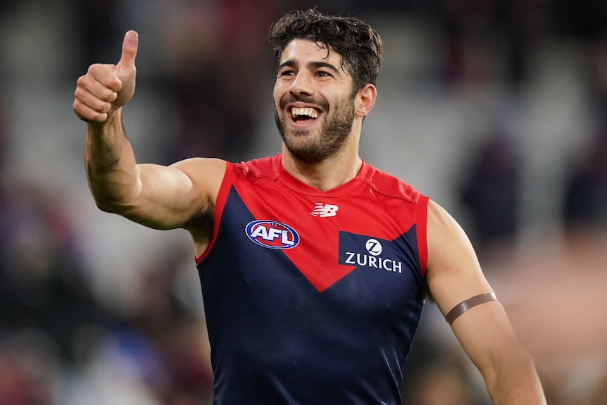 A Melbourne Demons AFL player smiles and gives the thumbs up with his right hand to the crowd.