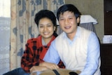 A young Xi Jinping, wearing white vest over a blue shirt, cuddles with Peng Liyuan in a red jumper