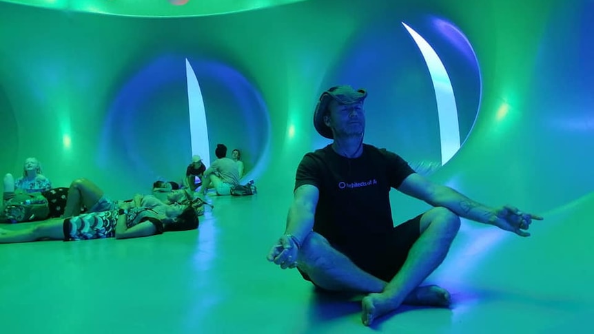 A man meditates inside an inflatable room with a green tone to the walls