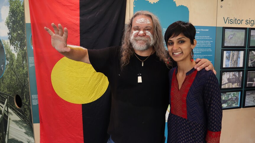 Indigenous Australian man and Indian woman stand next to each other smiling.