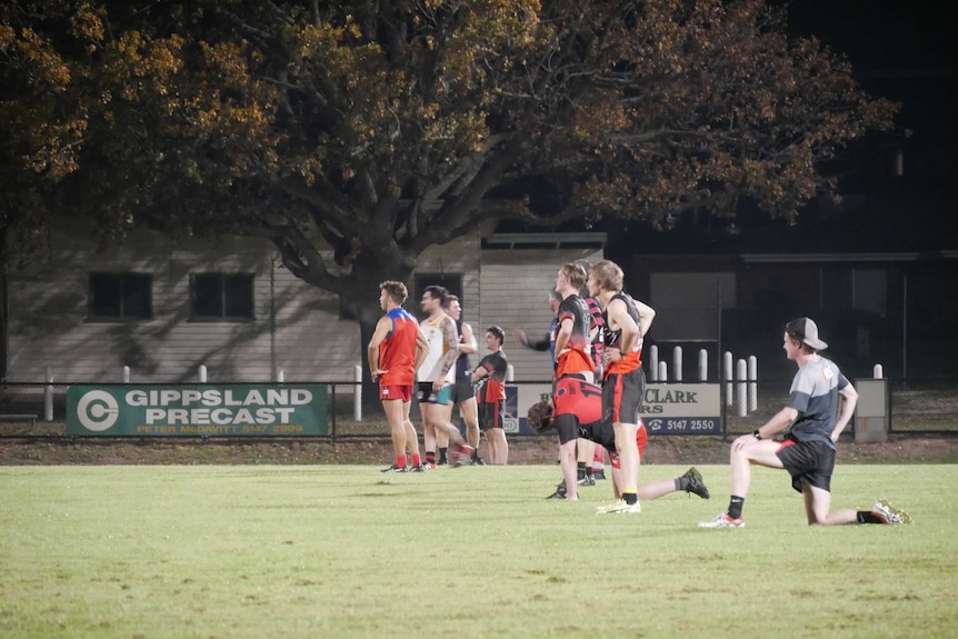 Two men stand apart from each other holding footballs