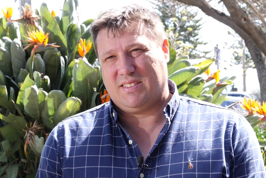 Foto en la cabeza y hombros del hombre frente a un arbusto de flores de naranja