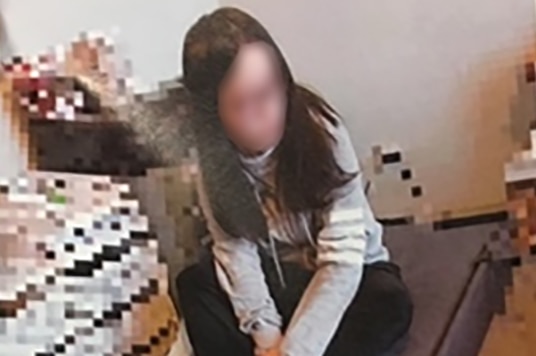 A woman, with face blurred, sits on the floor
