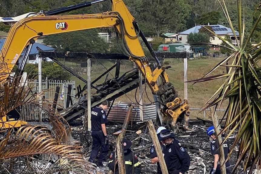 Police and fire investigators in uniforms looking through blackened rubble.