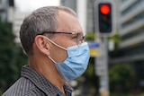 A man wearing a mask stands near a traffic light