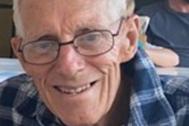 A profile image of a man with white hair, wearing glasses and a checked shirt, smiling.