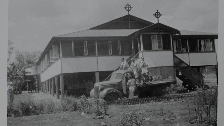 Black and white photo of building with two christian crosses on the roof with people on a car below in the driveway