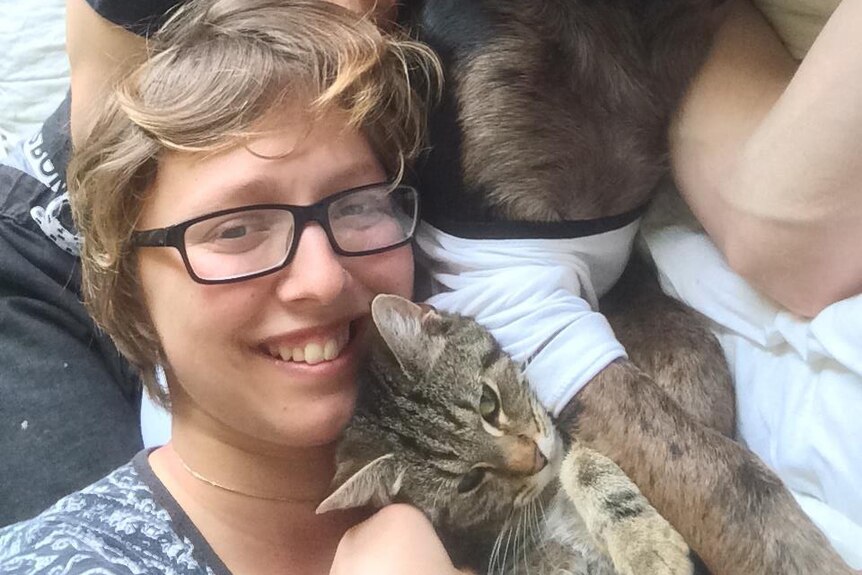 Cassandra lies back, holding onto a pet tabby cat.