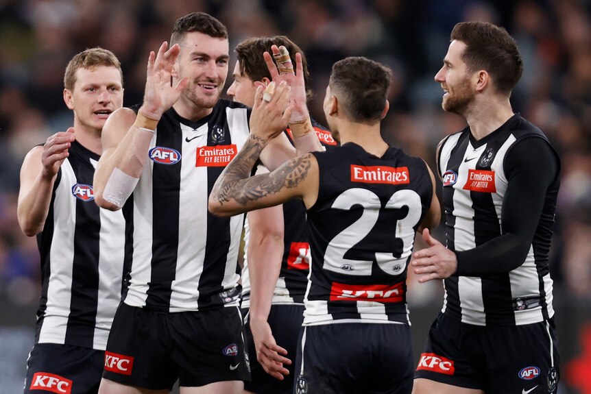 Collingwood players surround a smiling teammate who has kicked a goal.