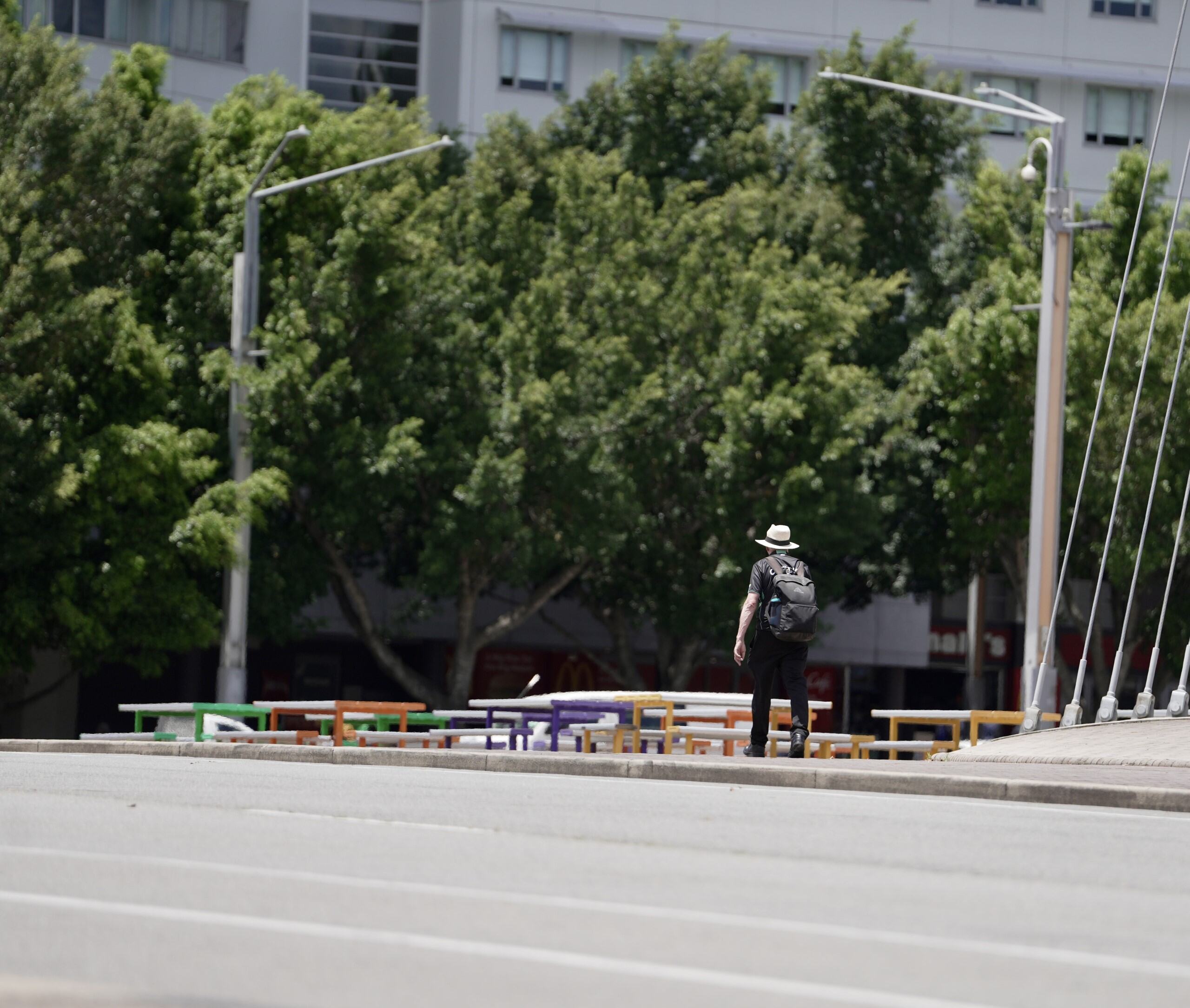 Person walks alone wearing dark clothes, white hat and a backpack.