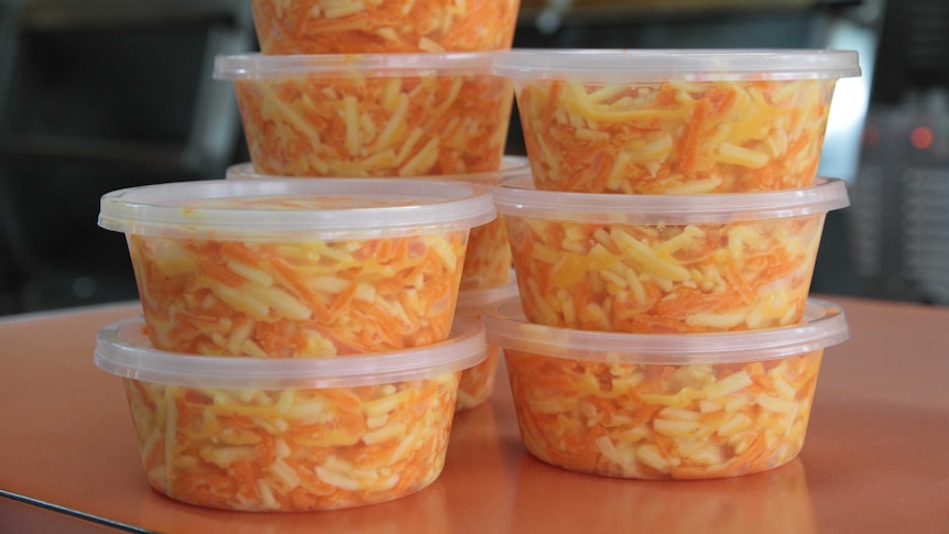 Tubs of cheese slaw stand stacked on a counter.