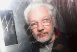 A photograph of Julian Assange through the window of what appears to be a police van.