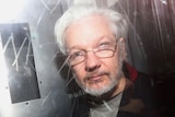 A photograph of Julian Assange through the window of what appears to be a police van.