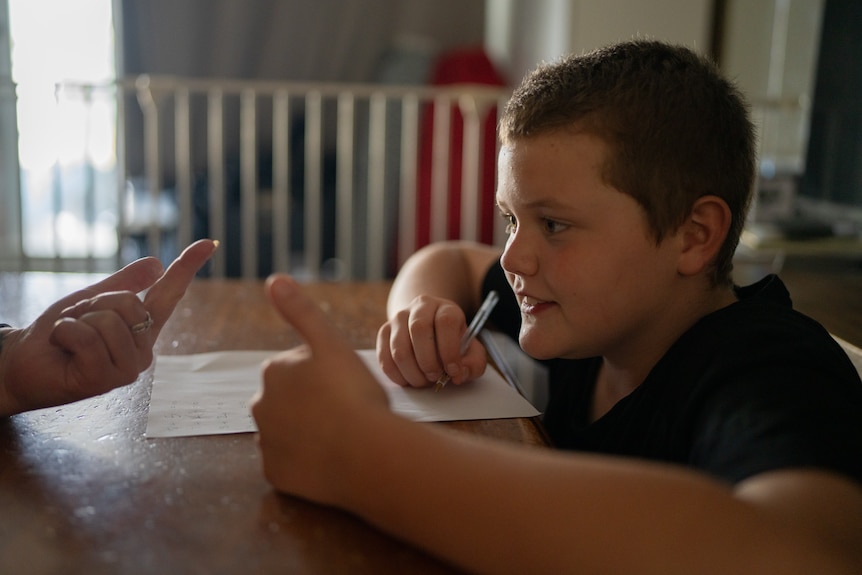 A boy sits at a table with a pen and paper in front of him.