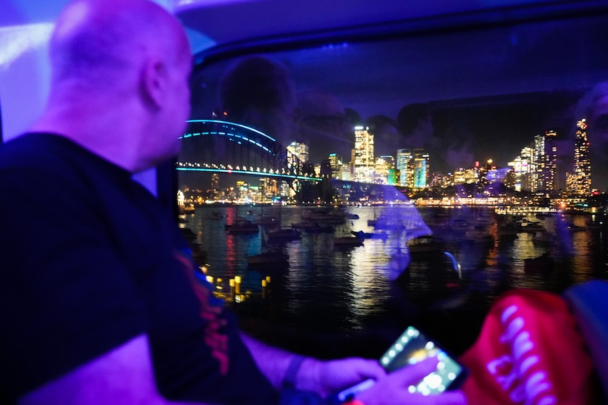Man bathed in blue light on Tekno Train looking at the view of Sydney CBD out the window