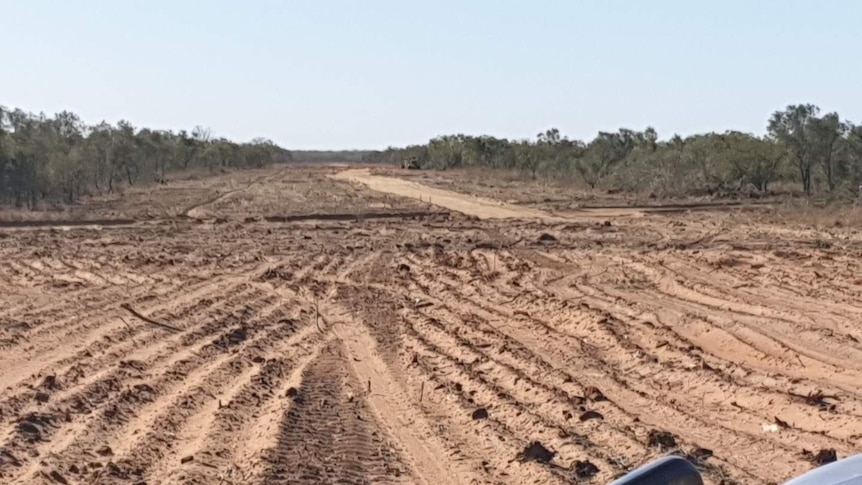 A large cleared area showing rough sand and dirt with a machine in the distance