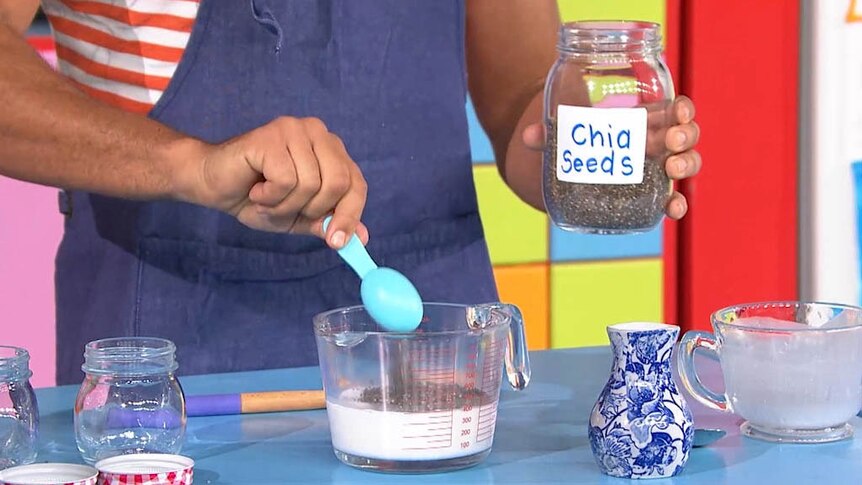 Table with someone holding a jar of chia seeds and while mixing chia seeds and coconut milk