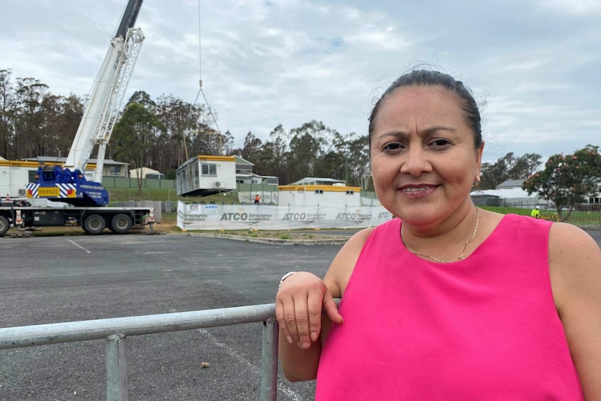 a woman in pink dress standing at fence near demountable buildings