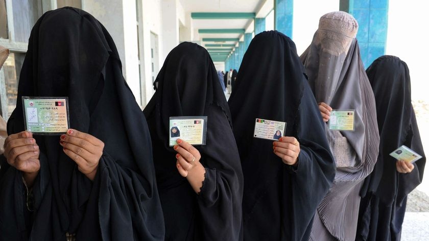 Burqa-clad Afghan women show identification cards as they wait to cast their votes