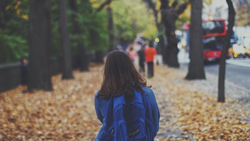 Girl walking to school in tree-lined street wearing a backpack