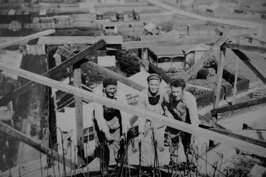 Monochrome image of three workers, high above houses on construction site scaffold.