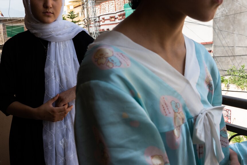 To women of the Hazara house stand on the balcony in colourful traditional dress. 