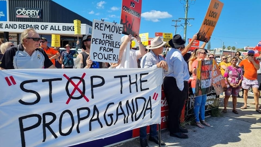 A rotund man stands in front of a number of protesters holding up signs at an anti-lockdown rally