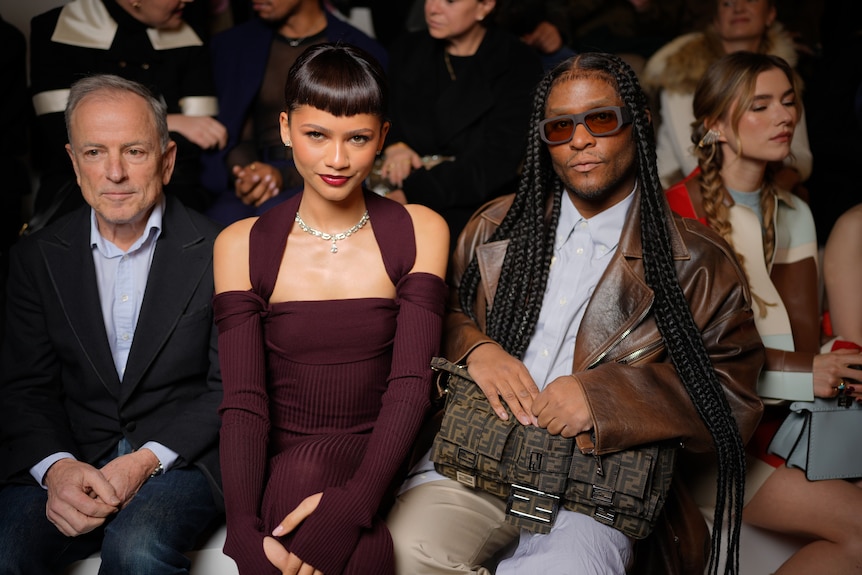 Zendaya, wearing a diamond necklace, sits next to Law Roach, in sunglasses, front row at a fashion show