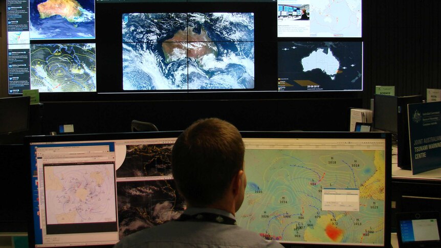 Man sitting in front of screens with satellite images in the background.
