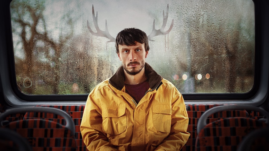 Donny stares into the camera as he sits at the back of a bus wearing a yellow jacket, with antlers photoshopped behind him.