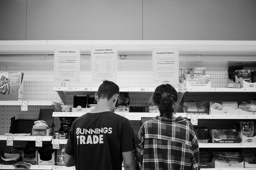 Man and woman stand at Coles shelves, in front of signs limiting the number of items shoppers can purchase.