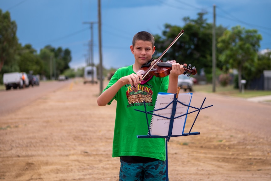 Thomas playing violin on a vast suburban Longreach street, November 2022.